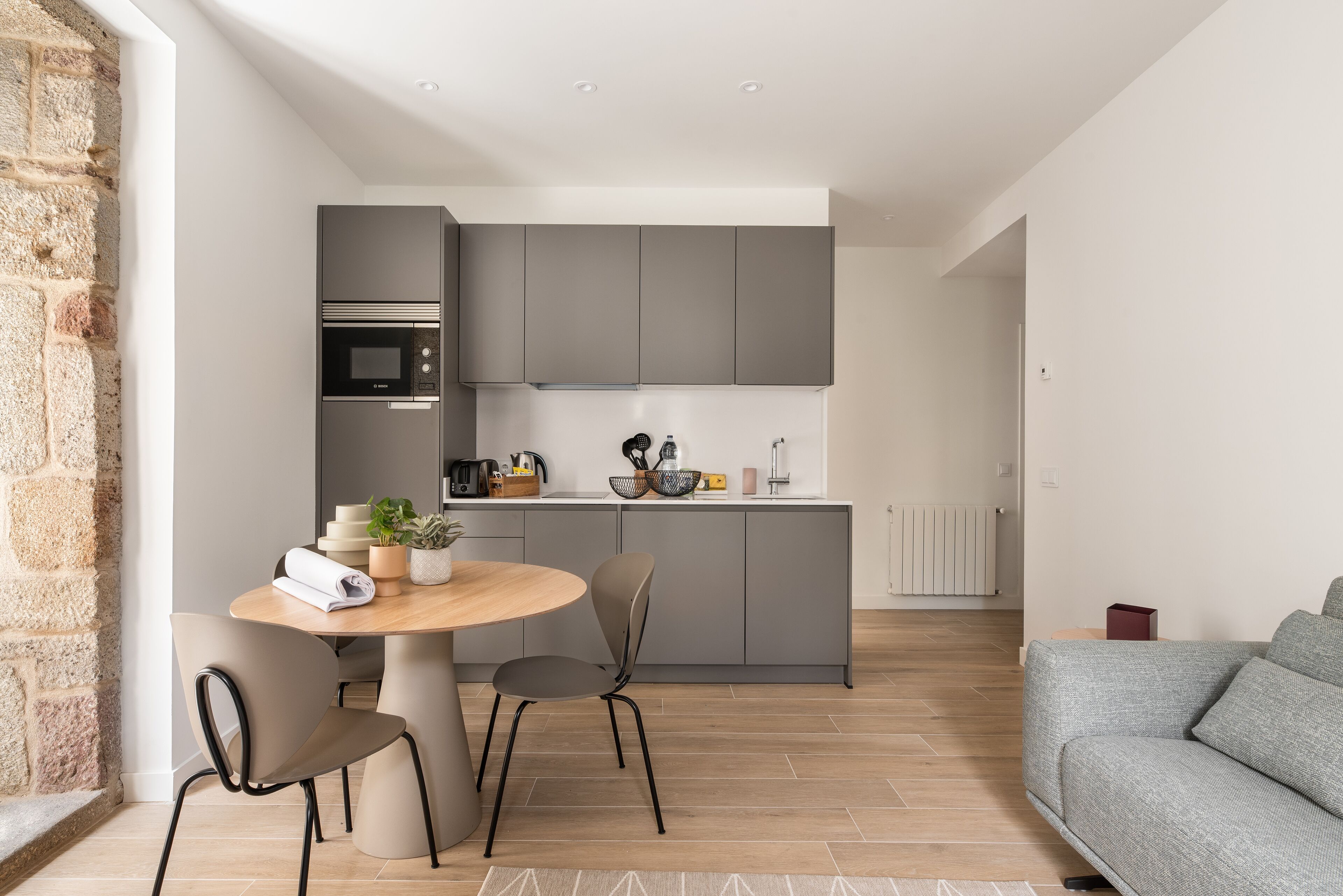 Una cocina moderna con gabinetes grises, un microondas integrado y un comedor con una mesa redonda y dos sillas.