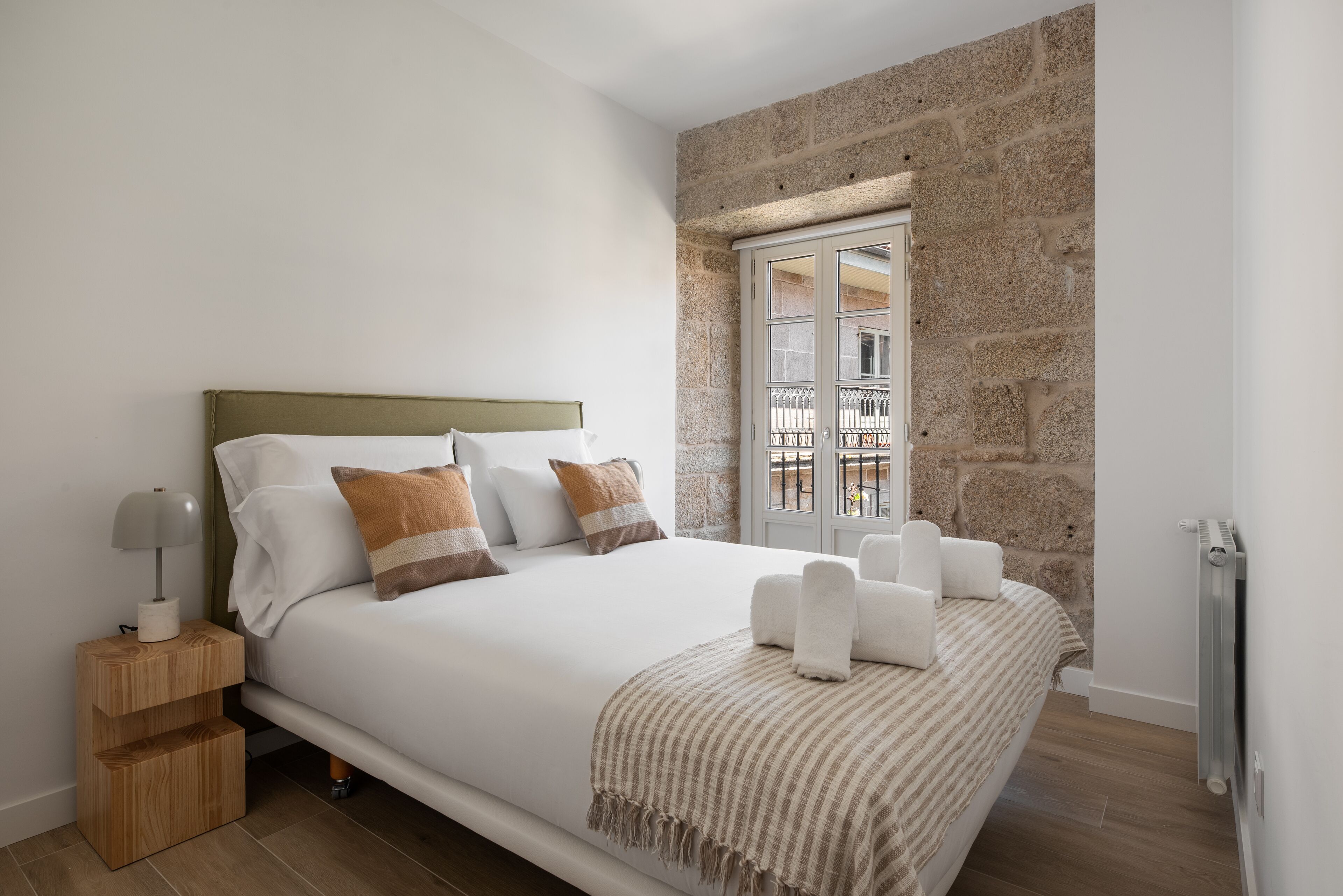 A bedroom with a bed, a nightstand, a window, and a stone wall.