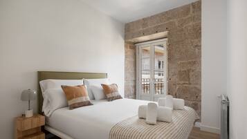 A bedroom with a bed, a nightstand, a window, and a stone wall.
