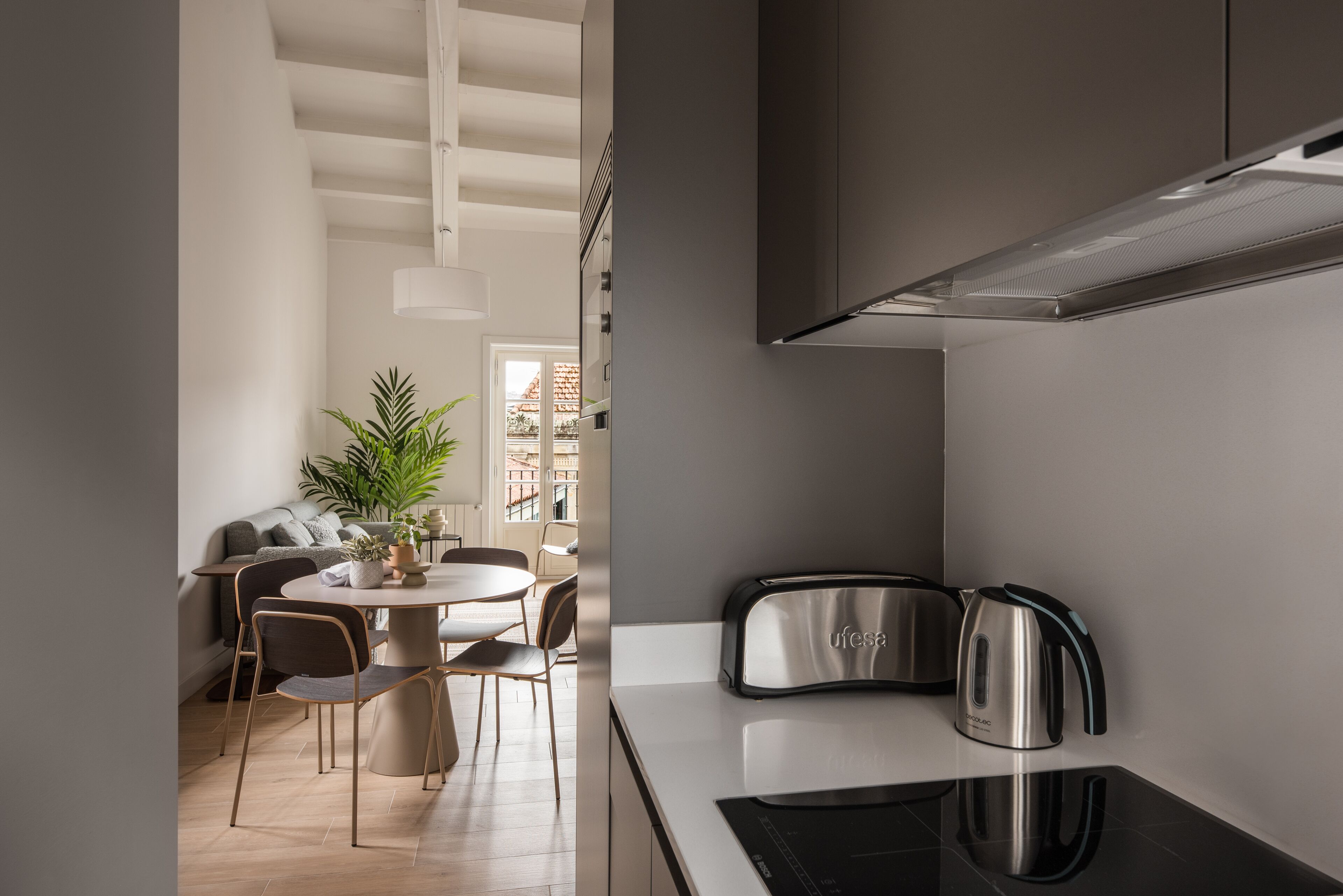 Una cocina moderna con horno empotrado, cafetera y comedor con mesa redonda y sillas.