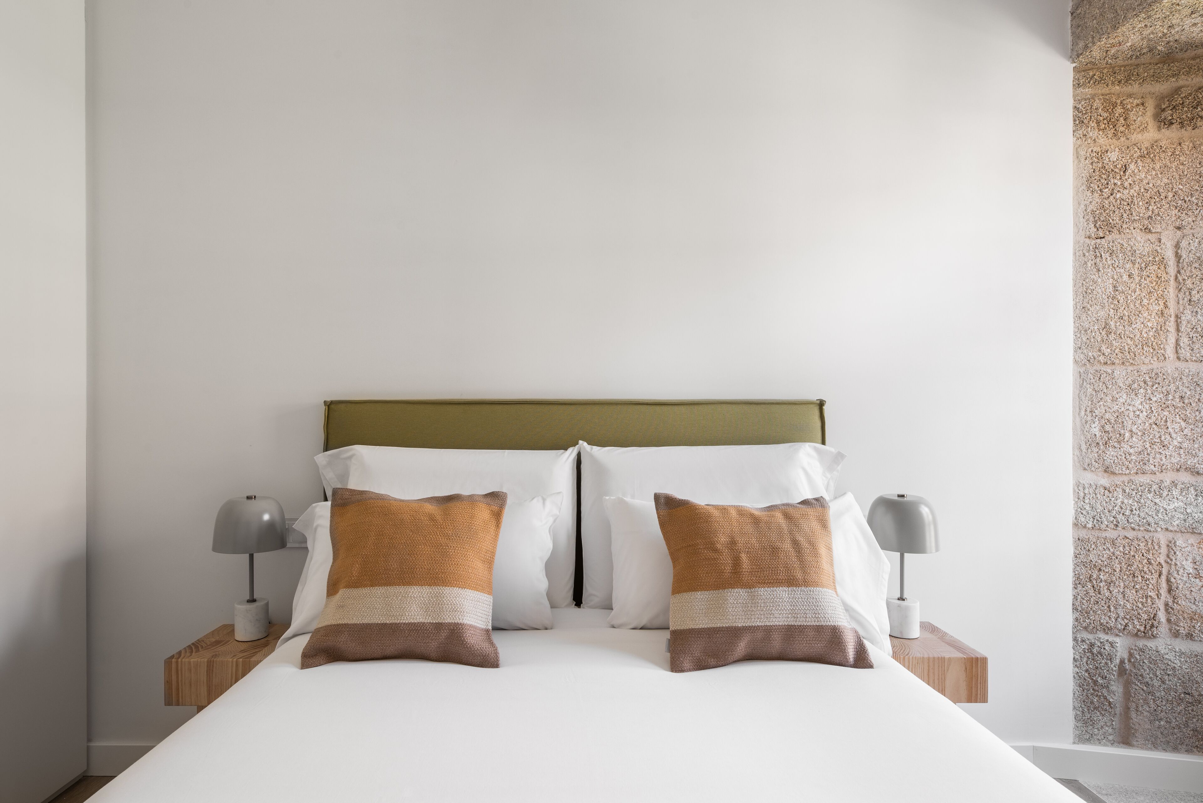 A neatly made bed with two pillows, a wooden headboard, and two bedside tables with lamps.