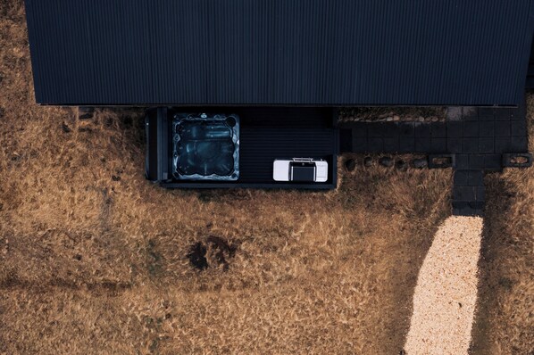 An aerial view of a building with a black roof, a gravel driveway, and a black container with a white object inside.