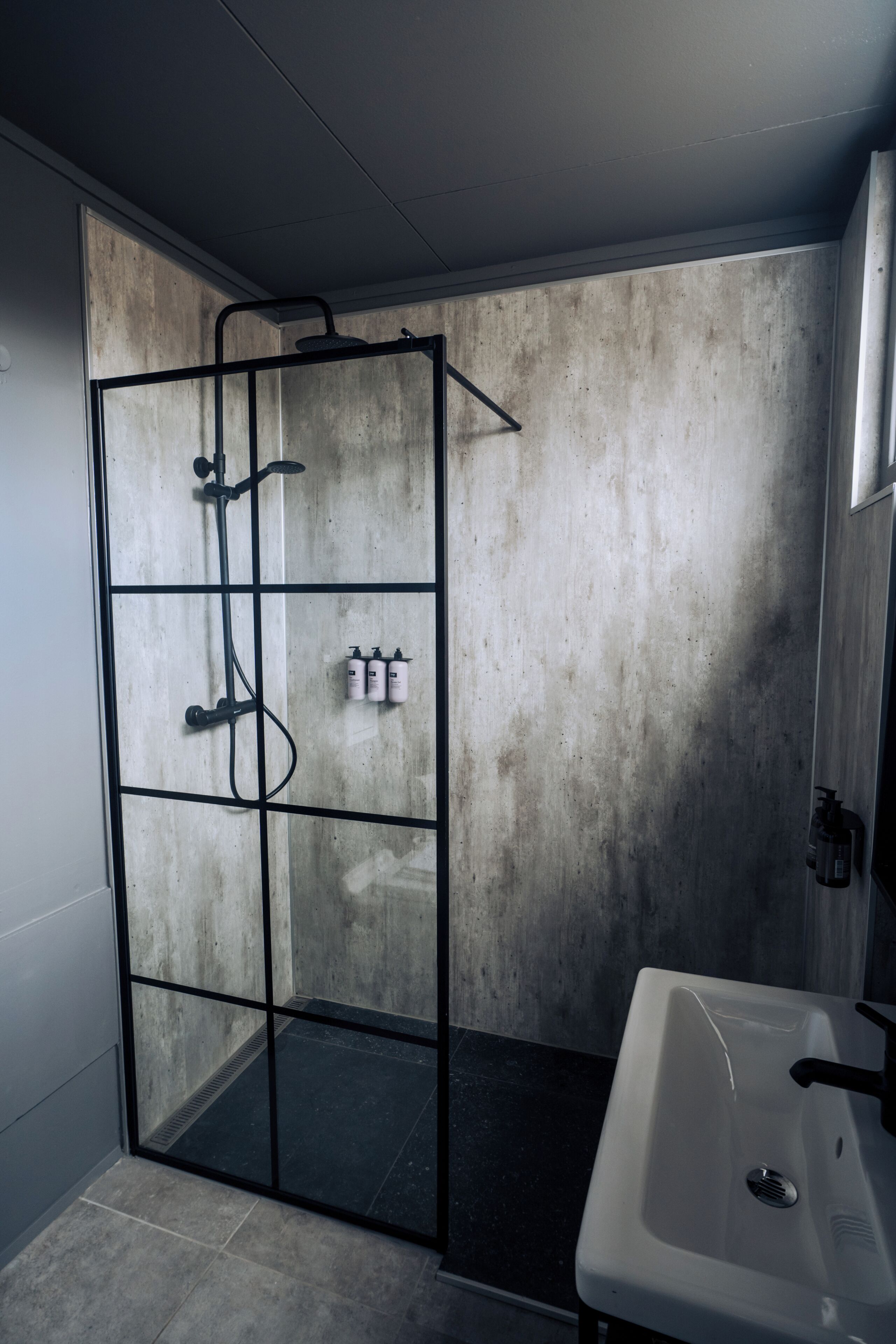 A bathroom with a glass shower enclosure, a white sink, and a concrete wall.