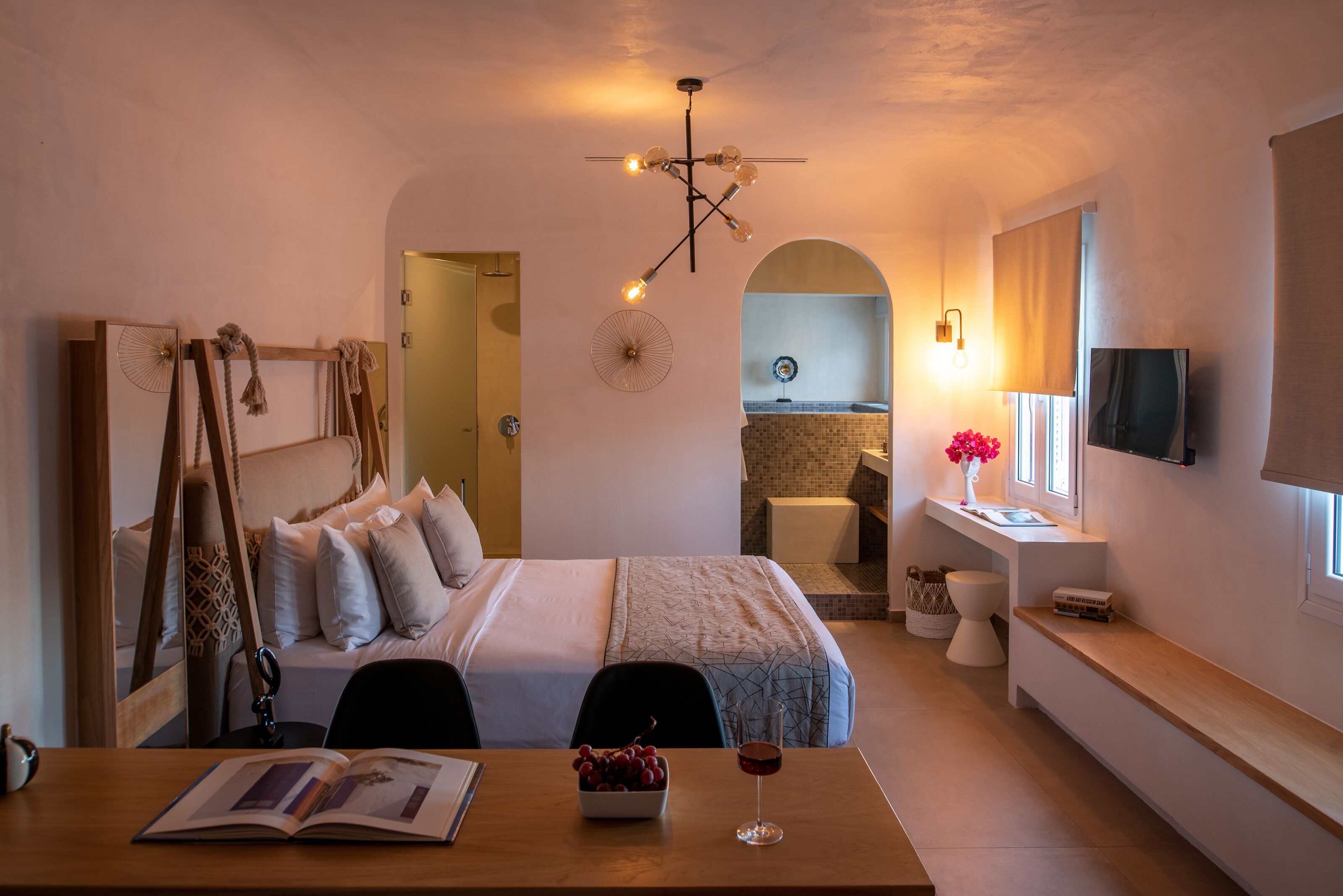 A hotel room with a bed, bedside table, reading material, and a dining area with a table and chairs.