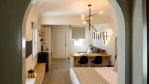 A narrow hallway leading to a bedroom with a bed, a desk with two chairs, a small kitchenette, and a ceiling light fixture. - Centro Santorini (Santorini)