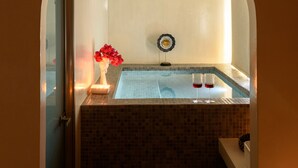 A spa area with a tiled pool, a decorative vase with red flowers, and two glasses of red liquid. - Centro Santorini (Santorini)