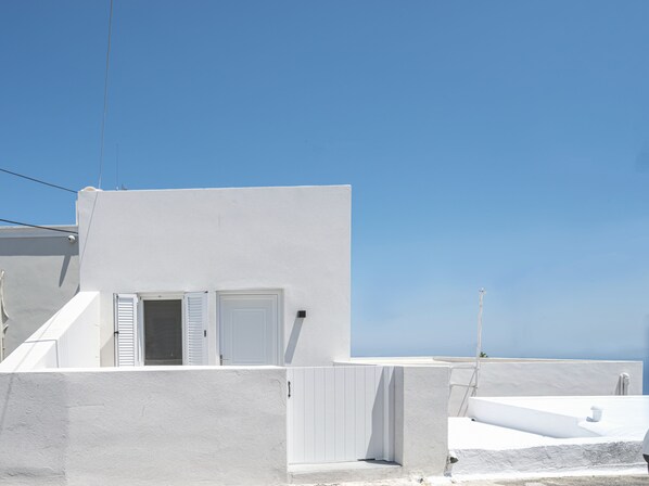 A white building with a door and windows, a white wall, and a clear blue sky. - Centro Santorini (Santorini)