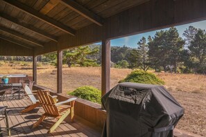Eine Terrasse im Freien mit Holzstühlen und einem Grill, mit Blick auf eine natürliche Landschaft mit Bäumen und blauem Himmel.