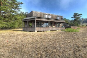 A two-story wooden house with a porch, surrounded by a grassy field and trees.