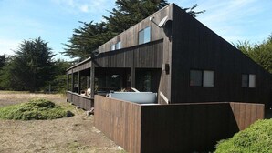 A modern two-story building with a wooden exterior, a covered outdoor area, and a large planter. - Seabbatical | Cozy Coastal Getaway with EV Charger (The Sea Ranch)