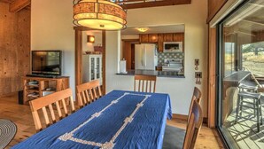 A cozy room with a wooden ceiling, a dining table with chairs, a television, and a kitchen area visible through an open door. - Seabbatical | Cozy Coastal Getaway with EV Charger (The Sea Ranch)