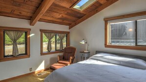 A bedroom with a large bed, a chair, a nightstand, and a skylight. - Seabbatical | Cozy Coastal Getaway with EV Charger (The Sea Ranch)