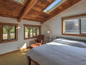 Ein Schlafzimmer mit einem großen Bett, einem Sessel, einem Nachttisch und einem Oberlicht.