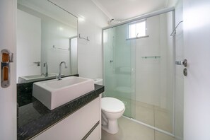 A bathroom with a white sink, a mirror, a toilet, and a glass-enclosed shower.