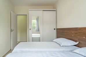 Ein Schlafzimmer mit Bett, zwei Kissen, einem hölzernen Kopfteil und einer Schiebetür, die auf einen Balkon führt.