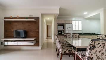 Cozinha moderna com eletrodomésticos embutidos, área de refeições com cadeiras estampadas e uma TV em uma prateleira de madeira.