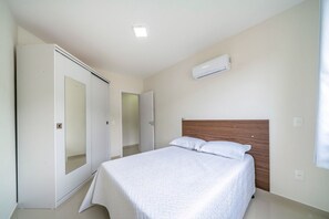 A bedroom with a bed, a wardrobe, an air conditioning unit, and a door.