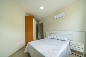 Un dormitorio con cama, mesita de noche, cajón, aire acondicionado y armario de madera.