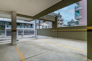 Un estacionamiento interior con suelo de concreto, líneas amarillas delimitando los espacios y una cerca blanca.