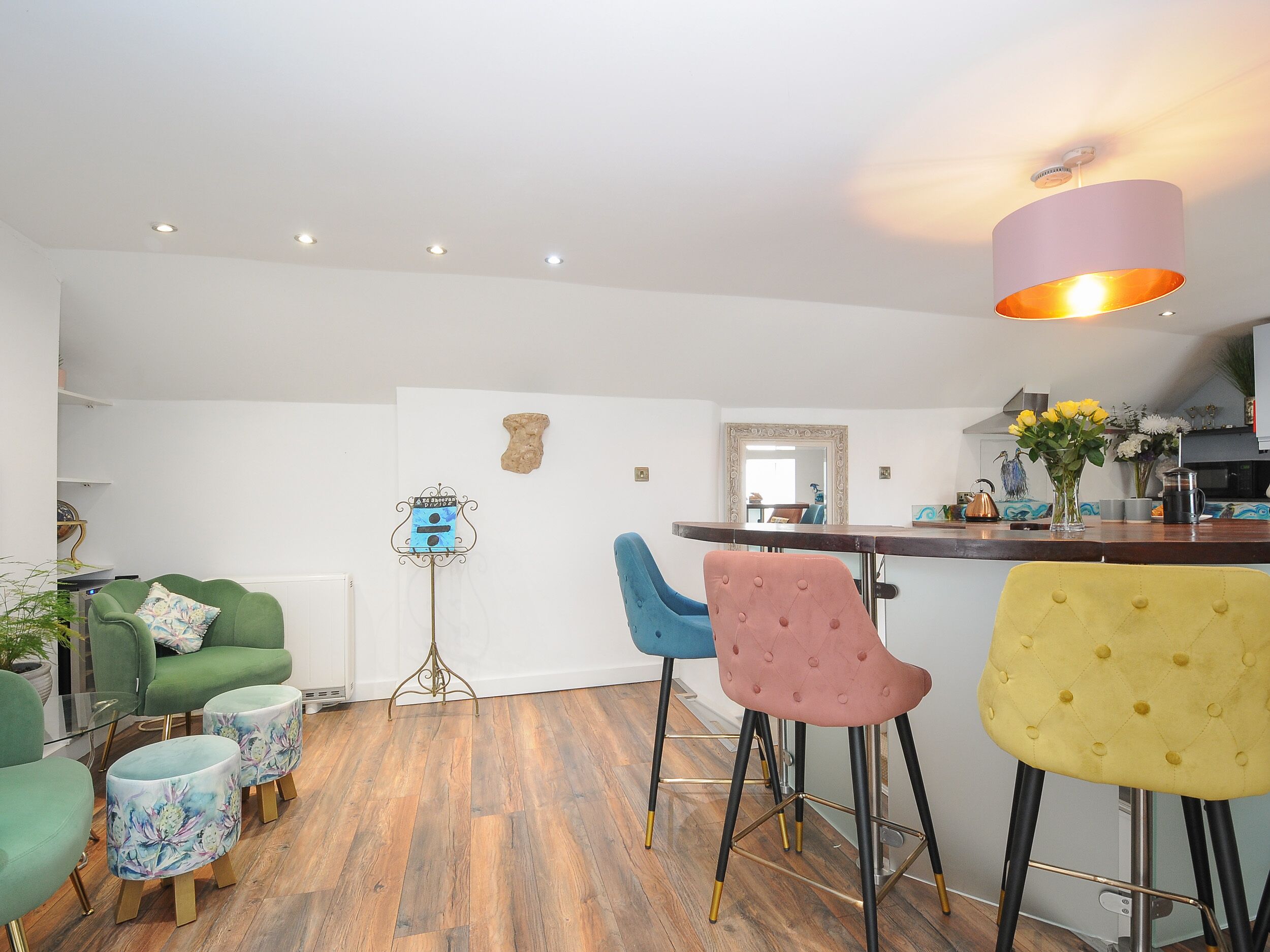 Una cocina moderna con barra, suelo de madera y taburetes de bar coloridos.