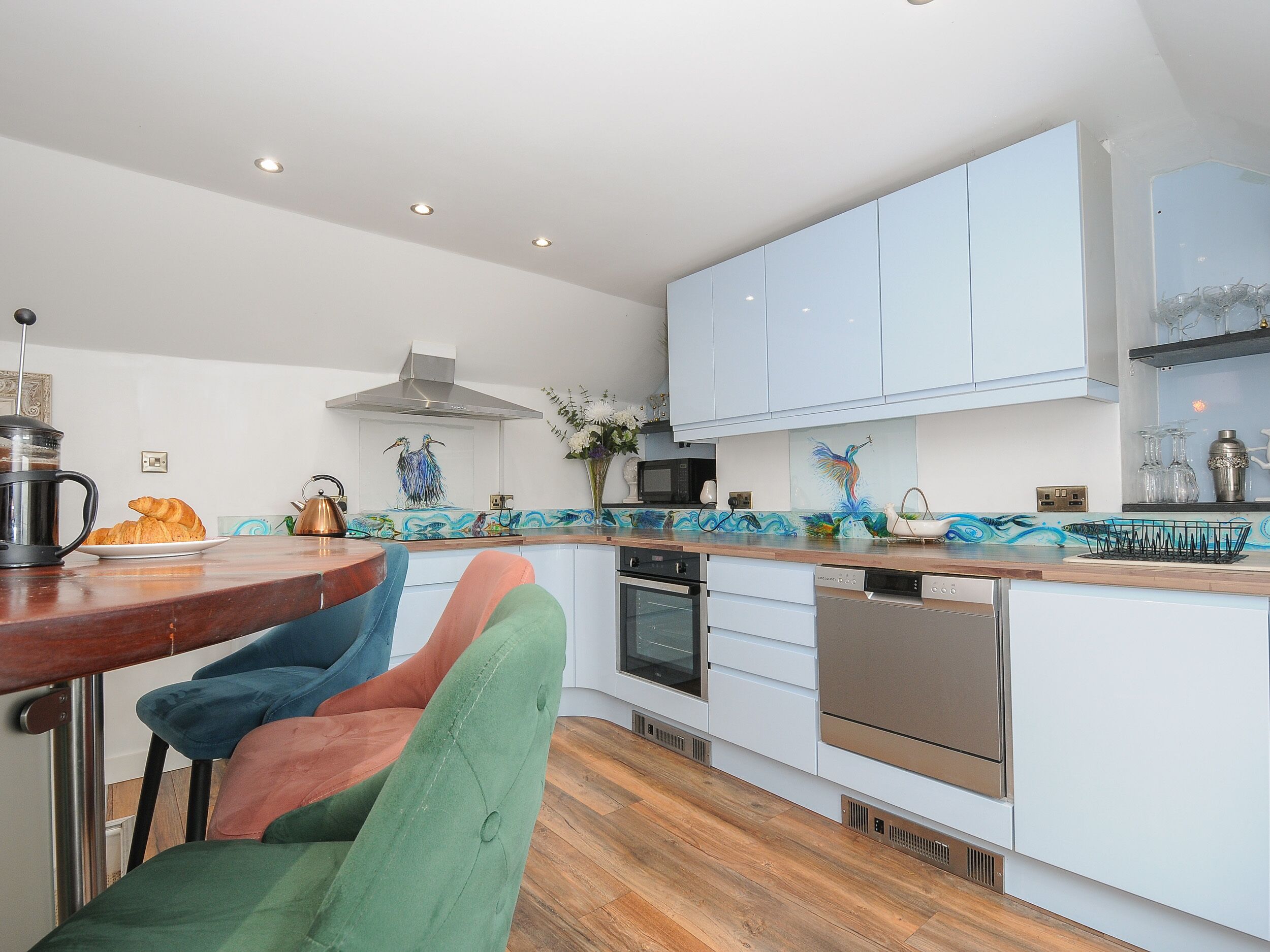 A modern kitchen with white cabinets, a wooden countertop, and a colorful backsplash.