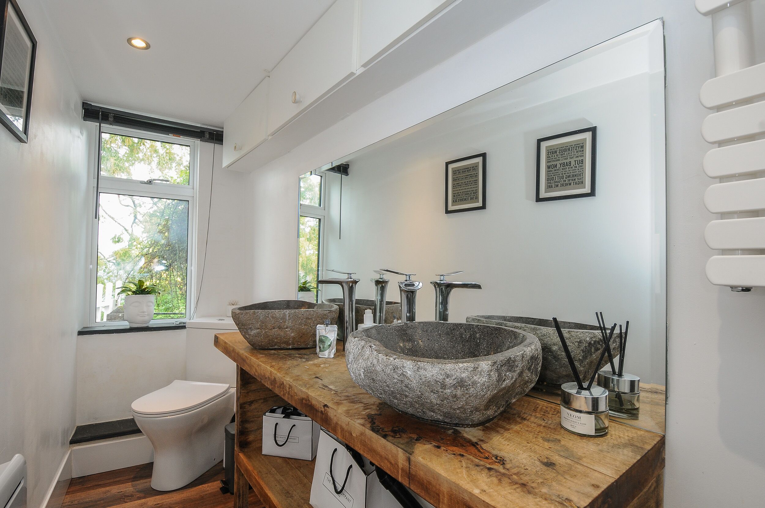 A modern bathroom with a large stone sink, a toilet, and a window with a view of trees.