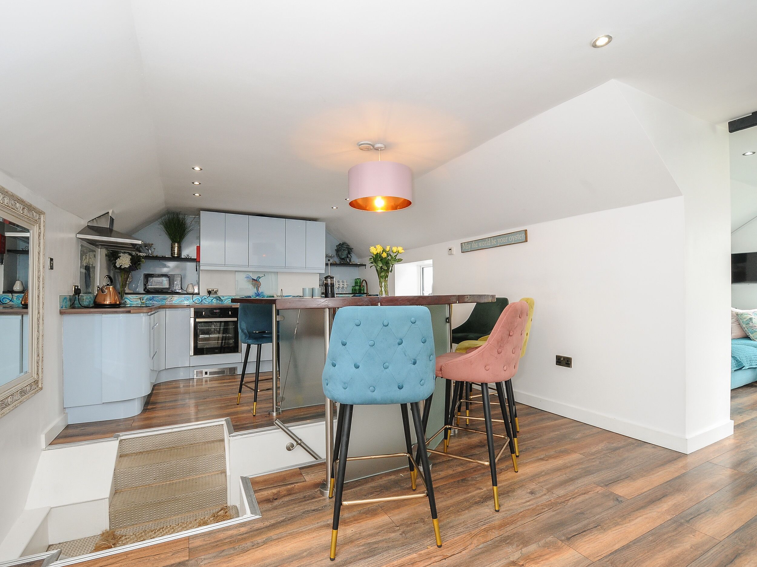Une cuisine moderne avec des meubles blancs, un îlot central et un luminaire suspendu rose.