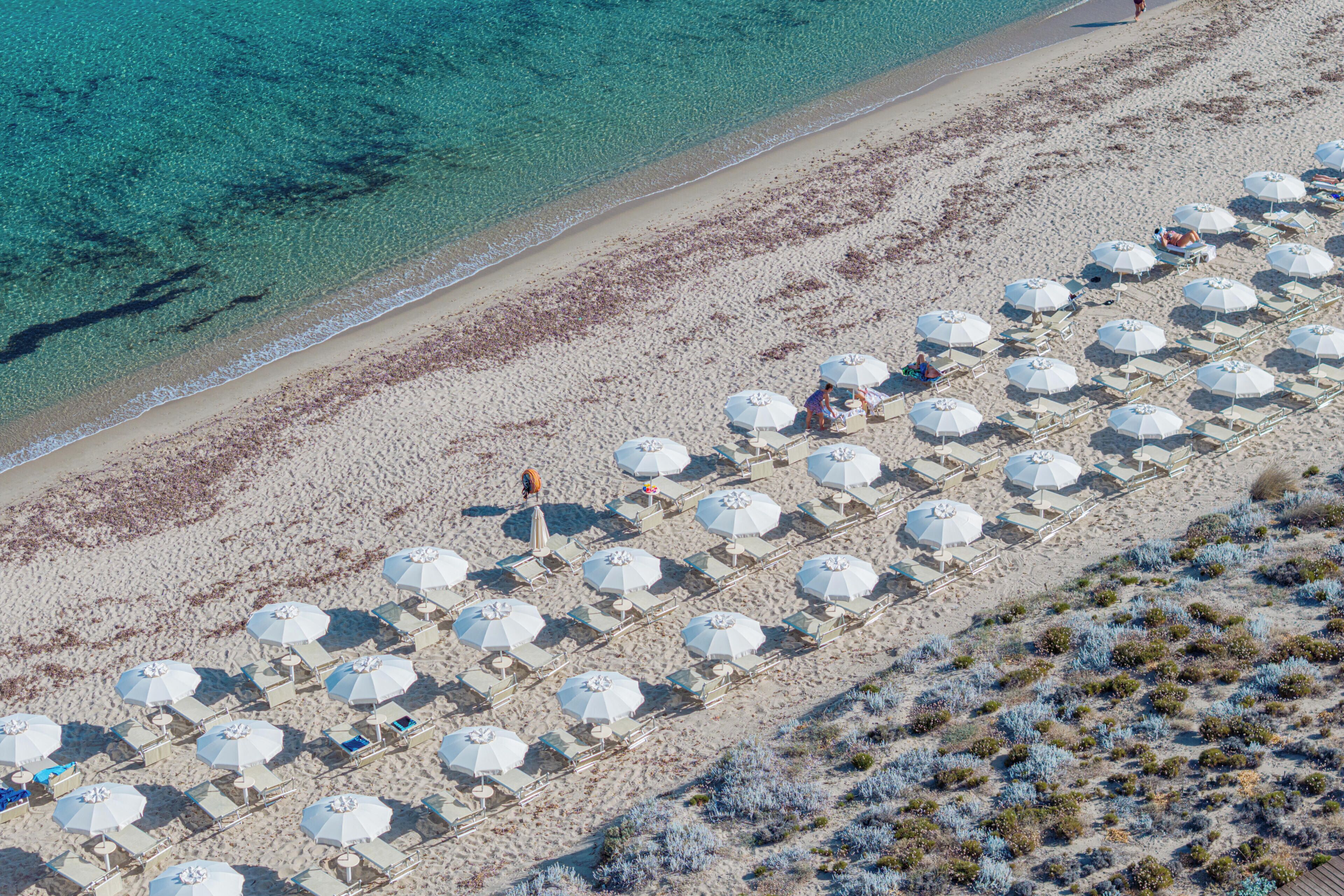 Luftaufnahme eines Strandes mit mehreren Reihen von Sonnenschirmen und Liegestühlen.