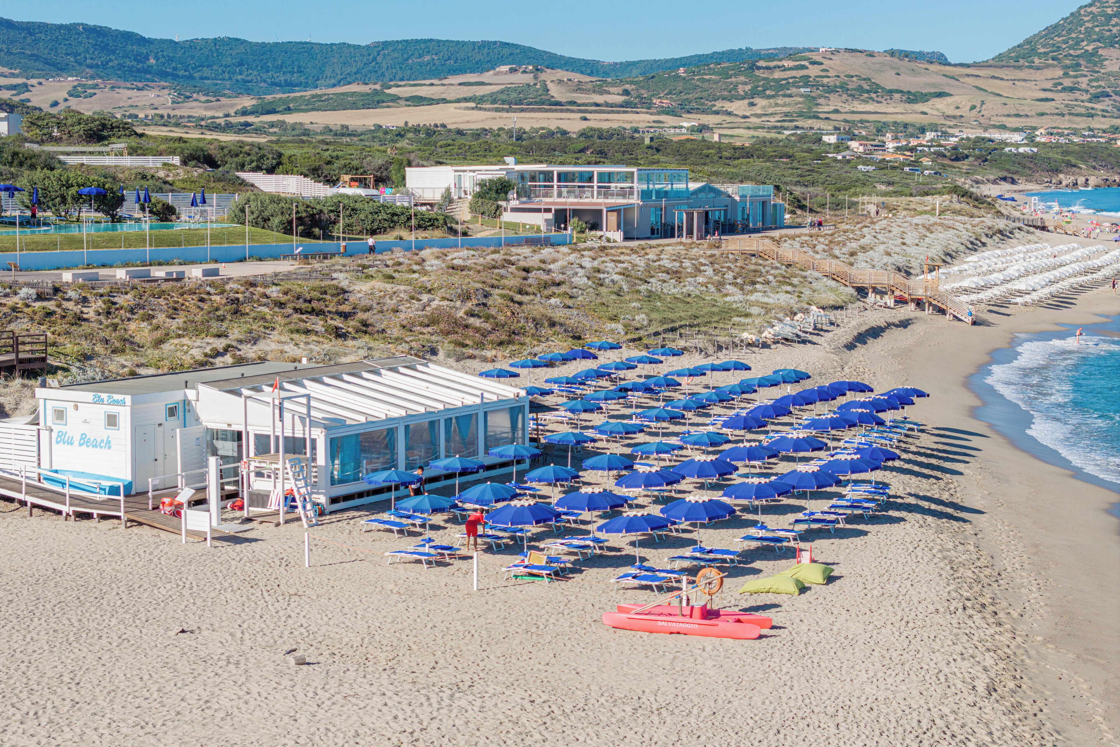 A beachside hotel with a pool, beach umbrellas, and a lifeguard tower.