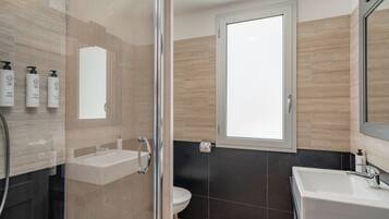 Un baño moderno con cabina de ducha de vidrio, un lavamanos blanco y un inodoro.