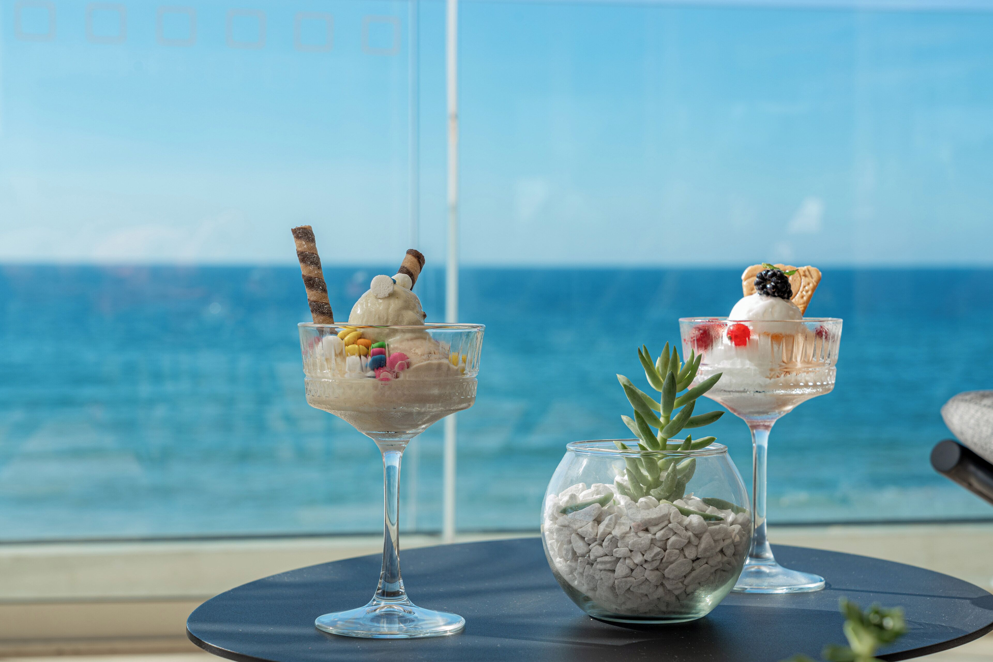 Tres vasos de postre sobre una mesa con vista al océano.