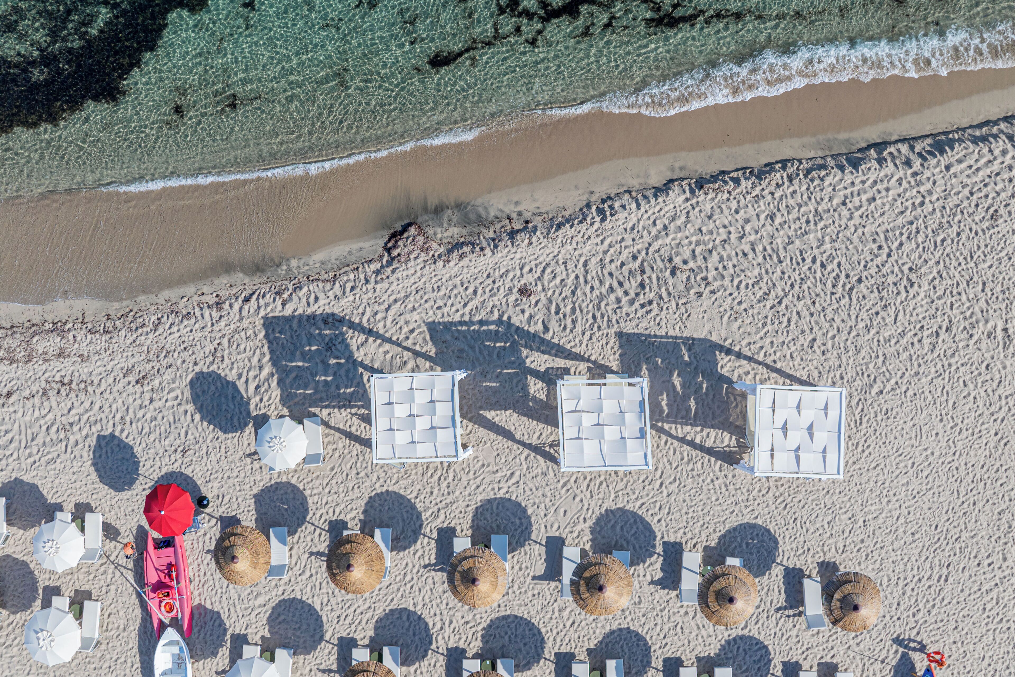 Vista aérea de una playa con sombrillas, sillas de descanso y un bote.