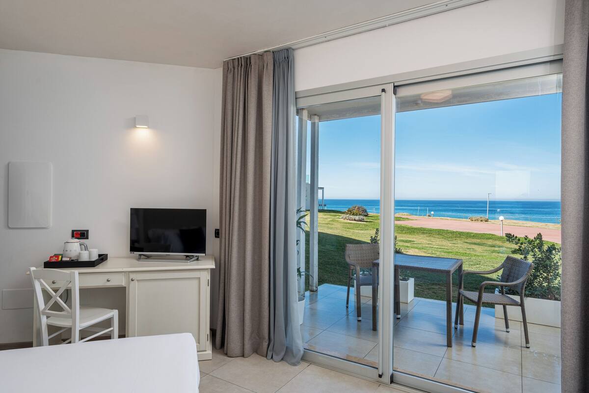 Une chambre d’hôtel équipée d’un bureau, d’une télévision et d’un balcon avec vue sur la plage.