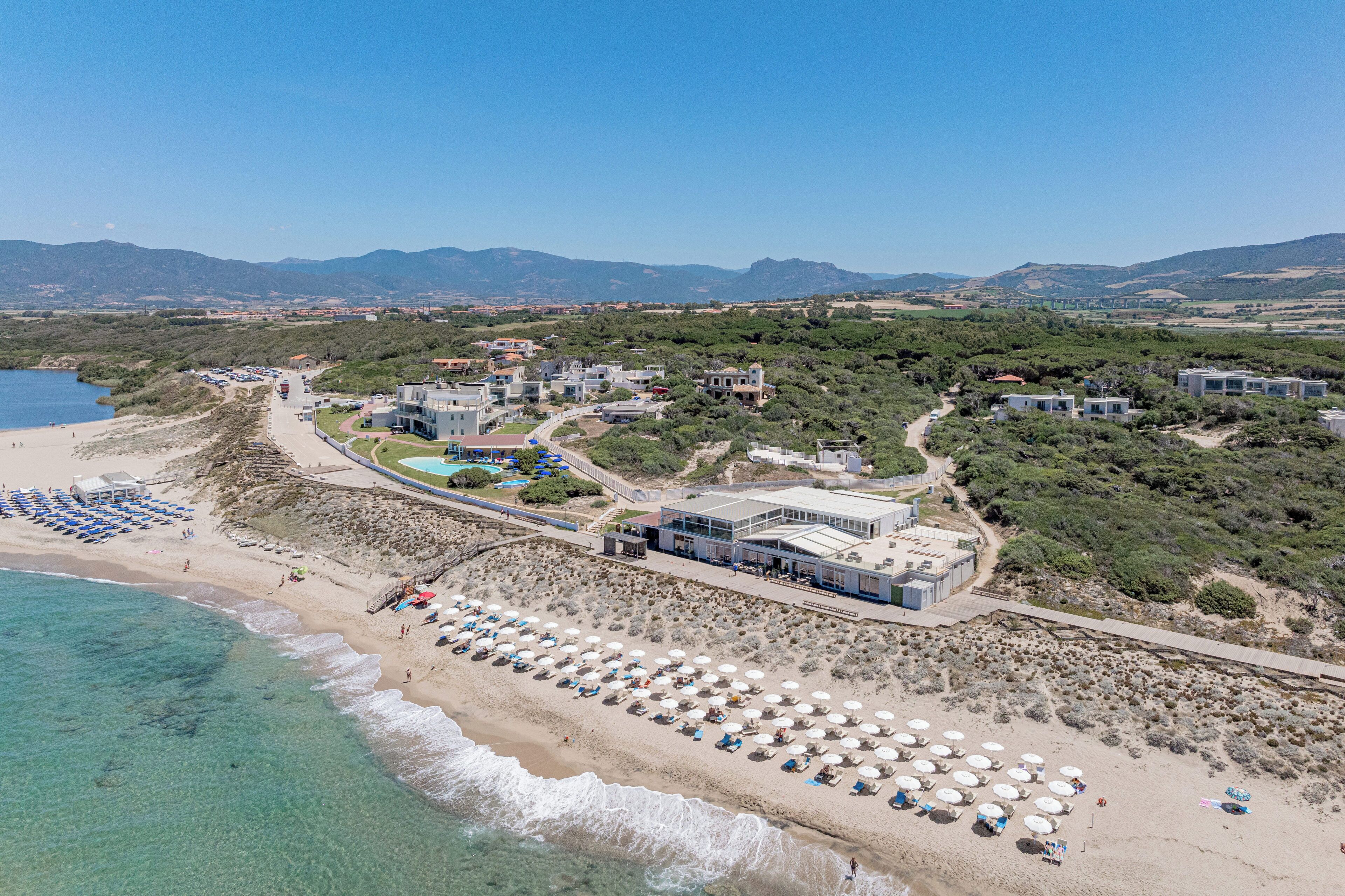 A coastal resort with beach umbrellas, a swimming pool, and buildings with a Mediterranean architectural style.