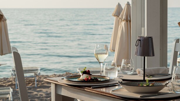 Una mesa de comedor con un postre, una copa de vino y una lámpara, con vista al mar.