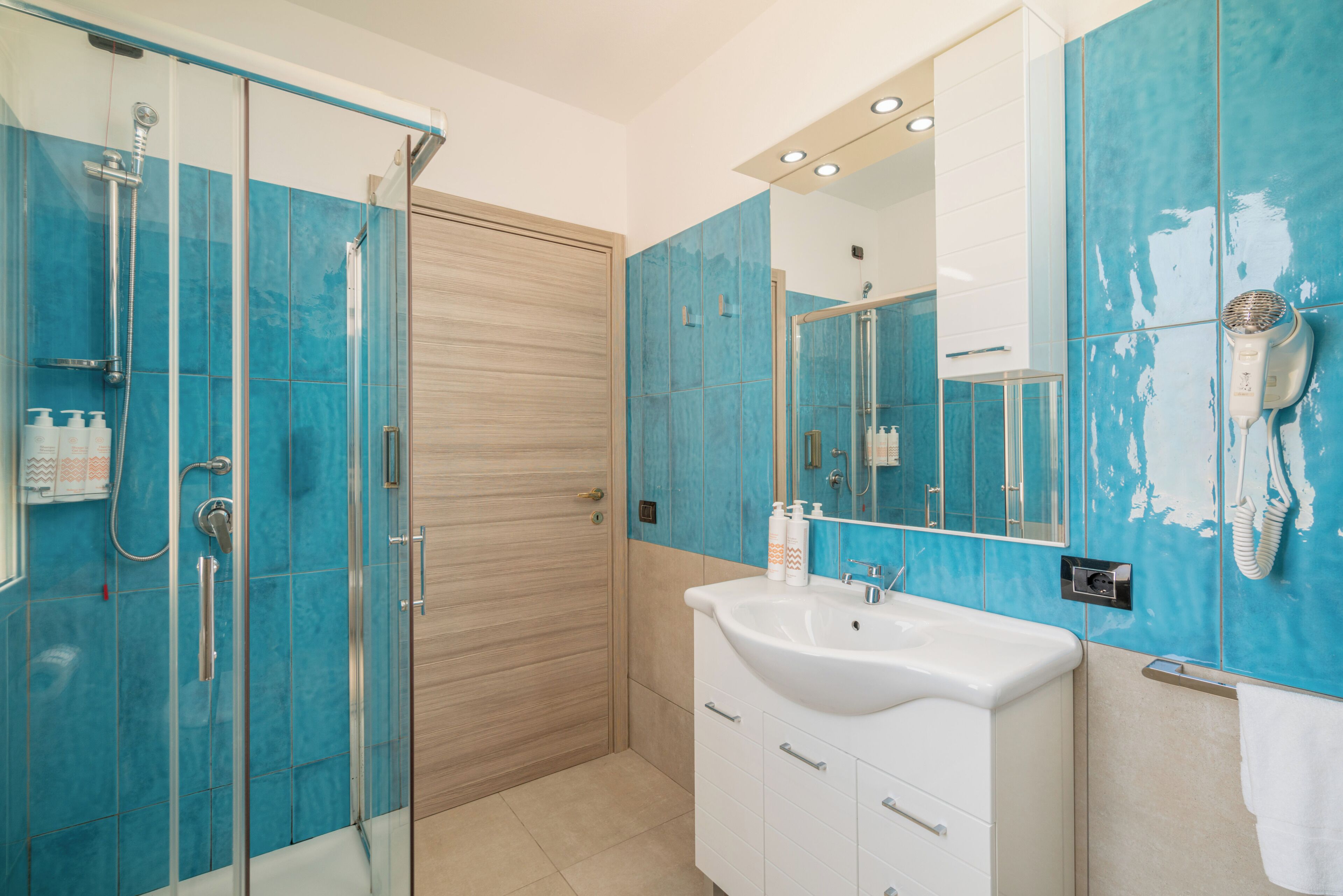 A bathroom with a glass shower enclosure, a white sink, and a mirror with a hairdryer mounted on the wall.