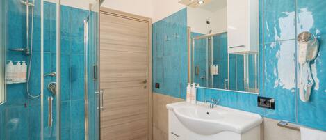 A bathroom with a glass shower enclosure, a white sink, and a mirror with a hairdryer mounted on the wall.