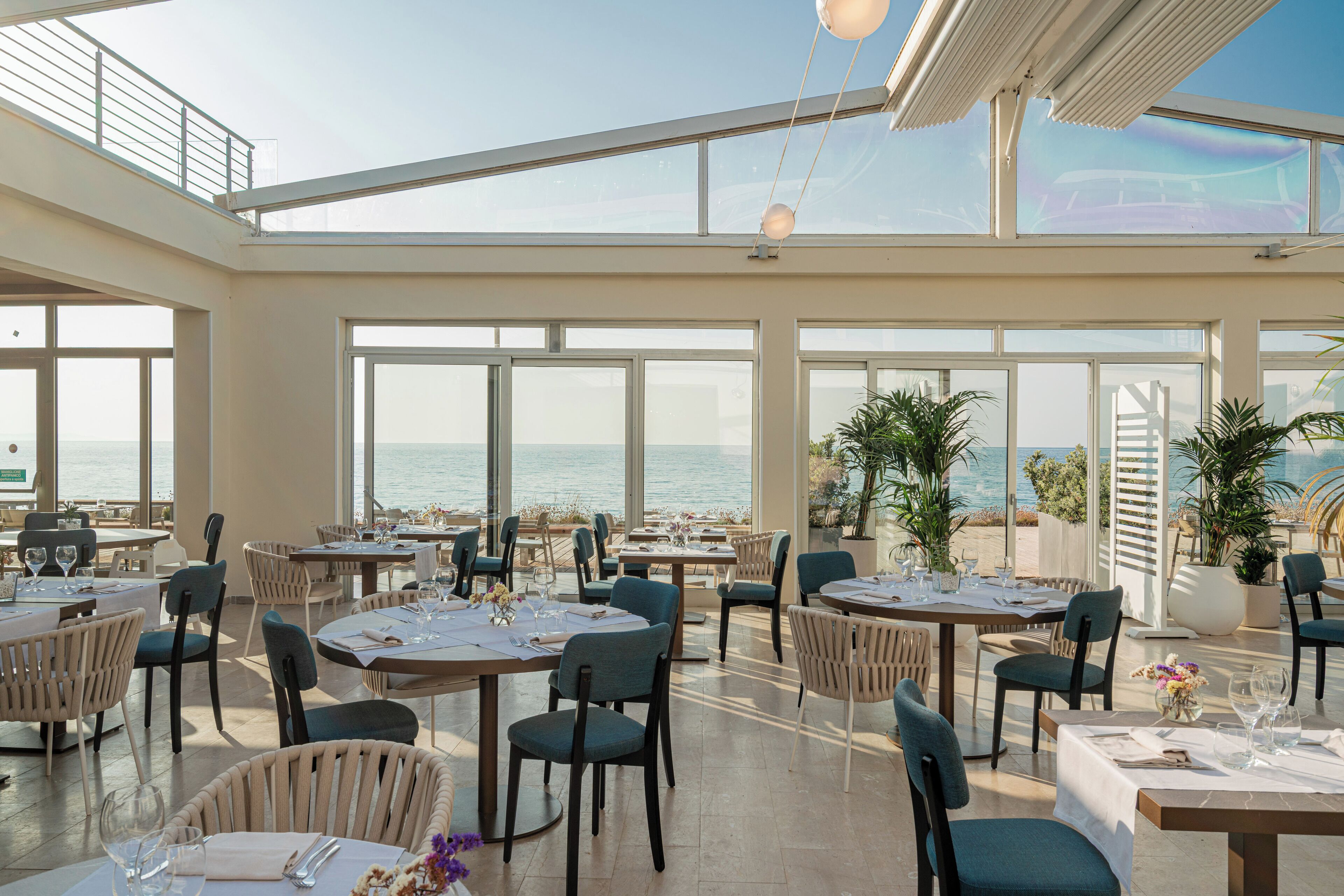 Un comedor espacioso con mesas y sillas, ventanas grandes y vista al mar.
