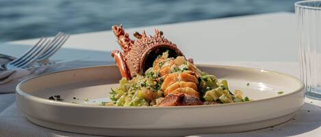 Een bord eten met een kreeftstaart, geplaatst op een tafel met uitzicht op zee.