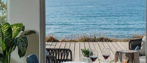 A dining table with a view of the ocean, a plant, and a glass of wine.