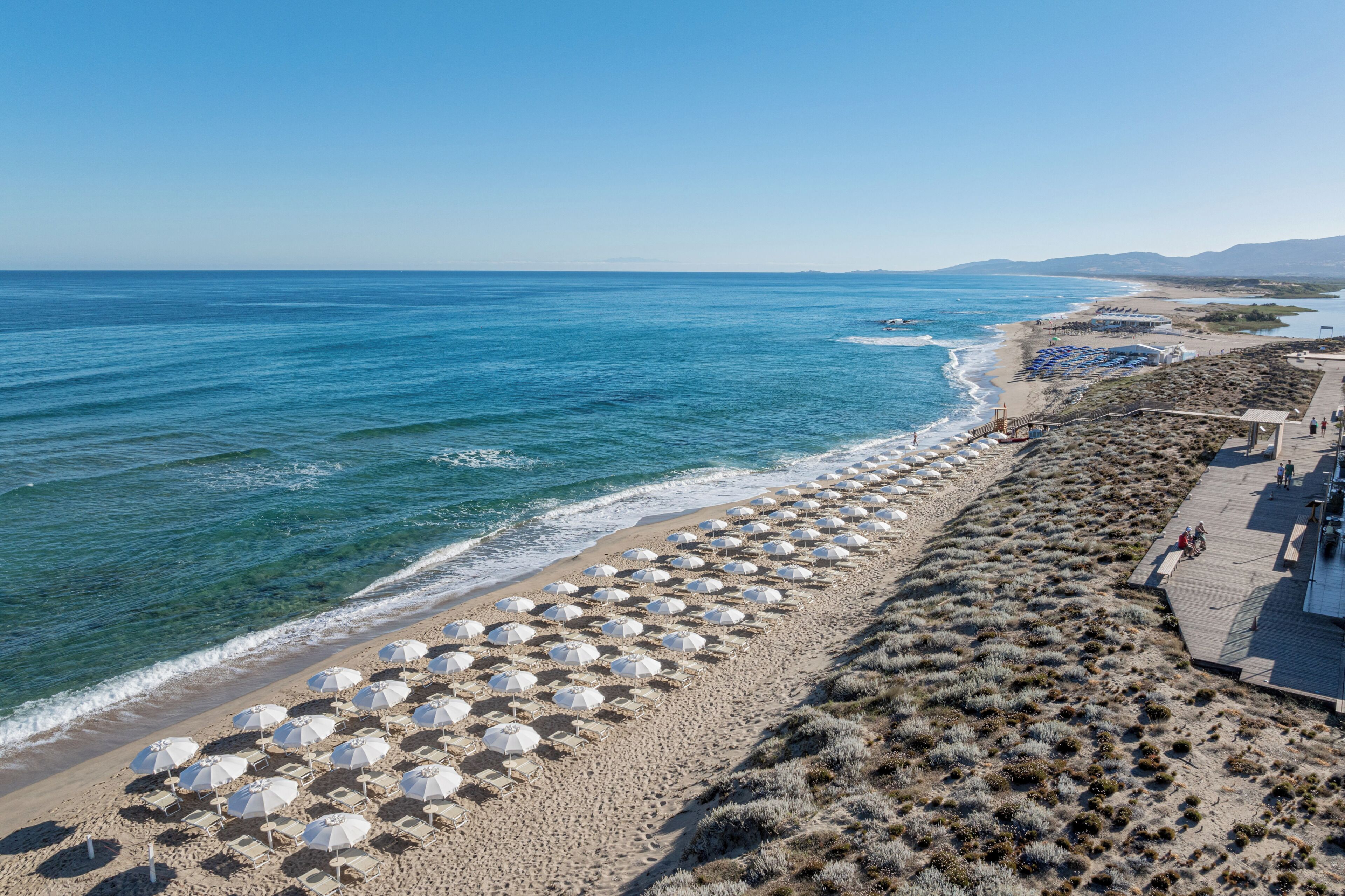 Una spiaggia con file di ombrelloni e una passerella di legno lungo la riva.
