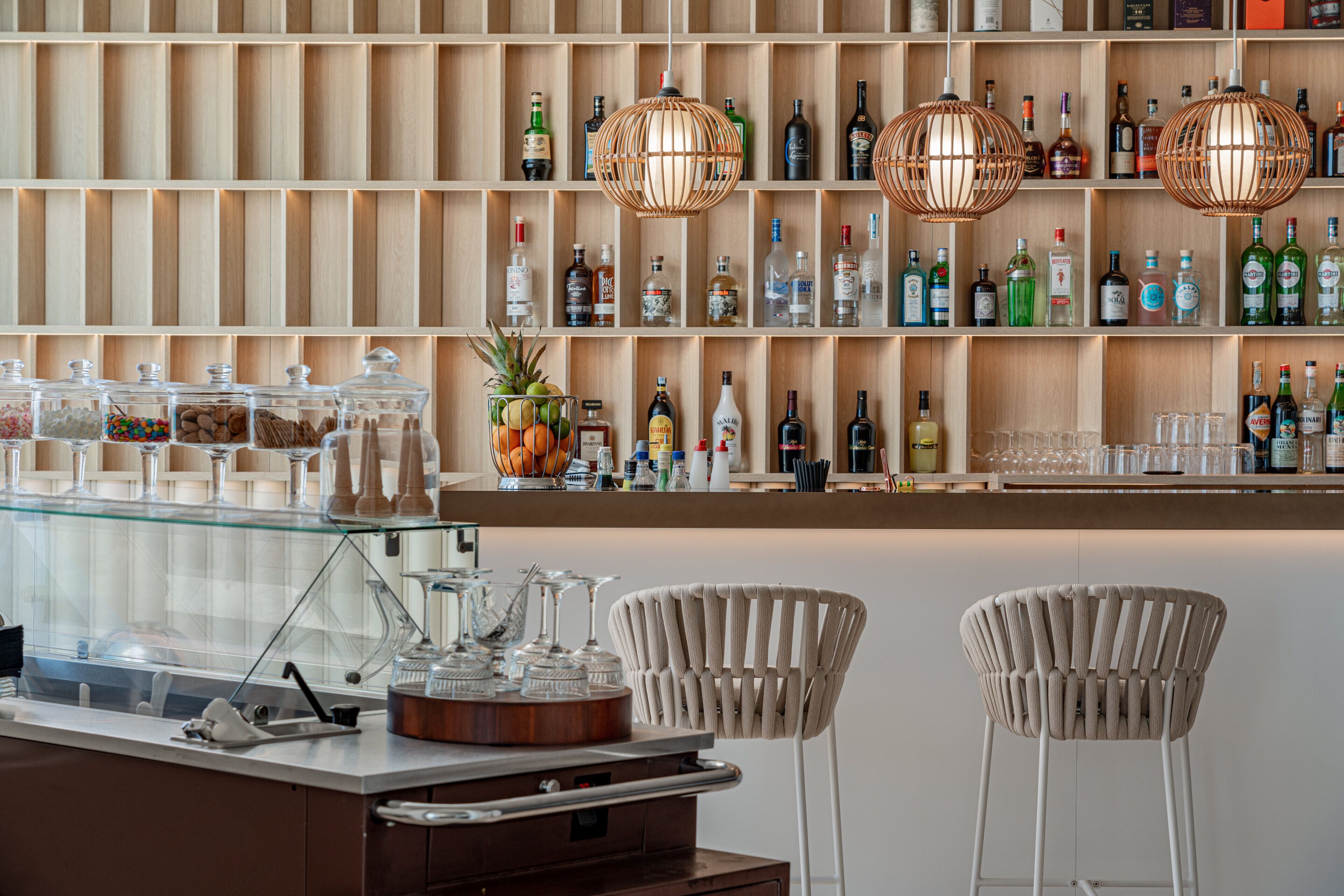 A bar area with shelves of liquor bottles, a glass display case with various items, and two wicker chairs.