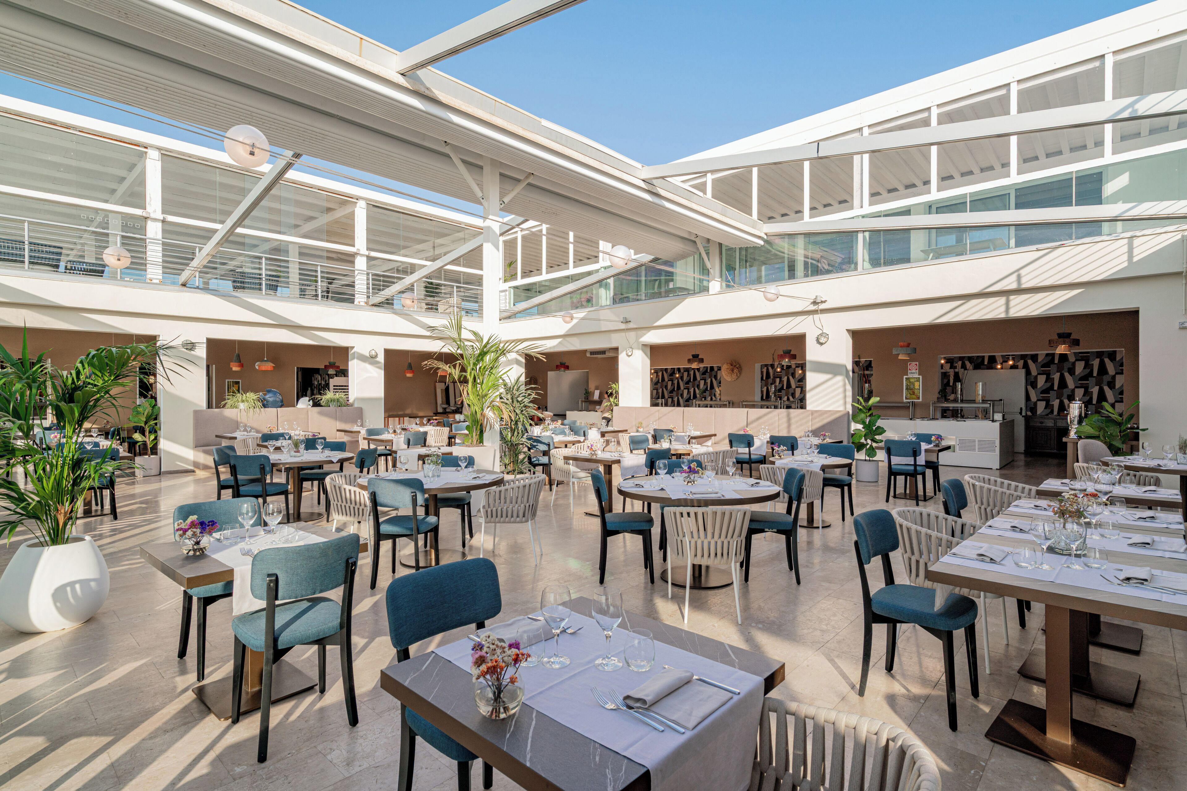 Un vaste espace de restauration intérieur, doté de nombreuses tables et chaises, de grandes fenêtres et d’un design architectural moderne.