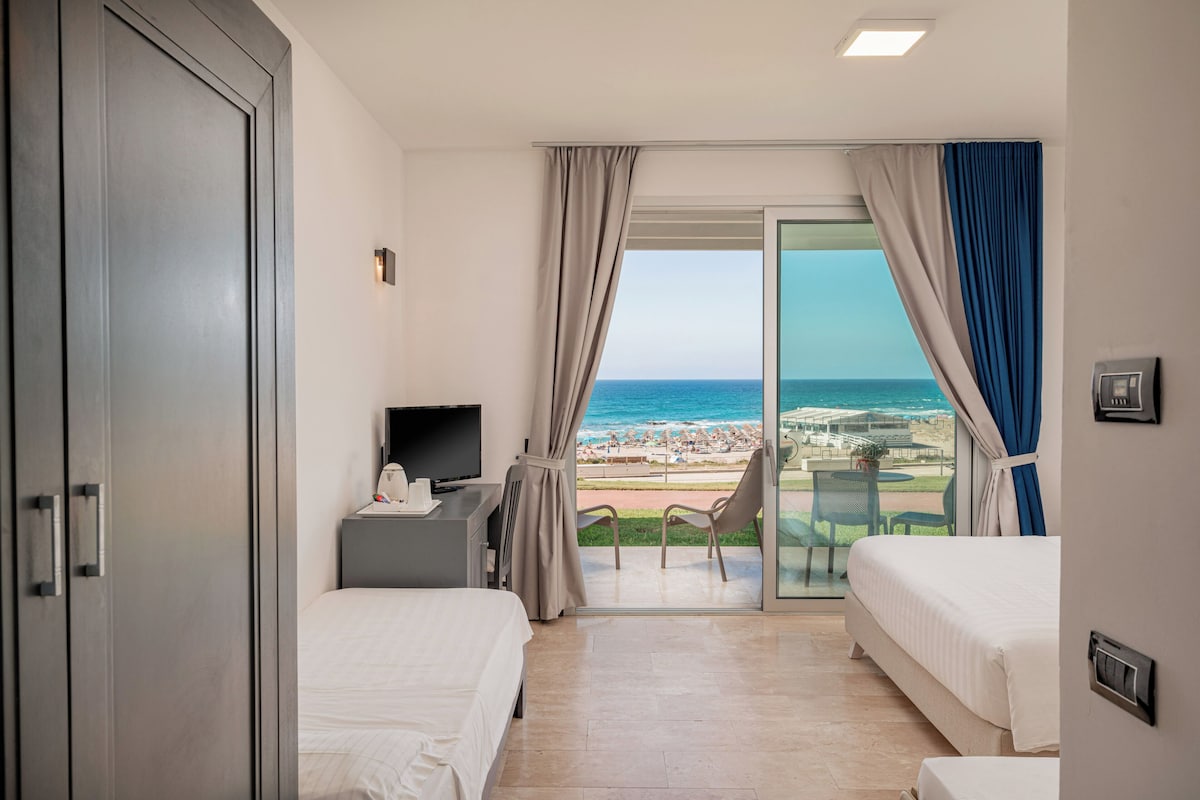 Une chambre d’hôtel avec deux lits, une télévision, un bureau et un balcon donnant sur la plage.