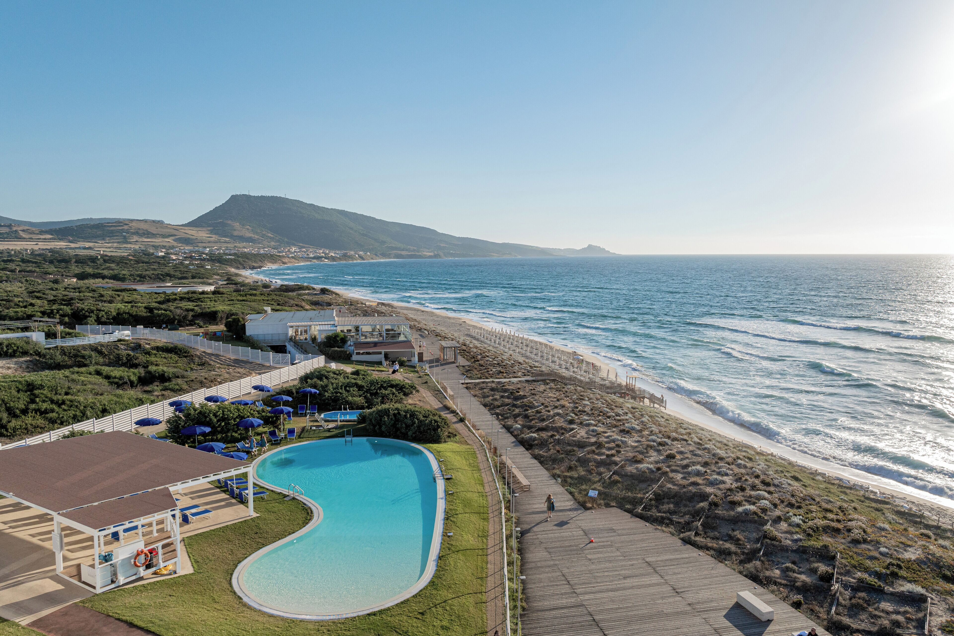A swimming pool adjacent to a beach with a view of the ocean and a mountain in the distance.