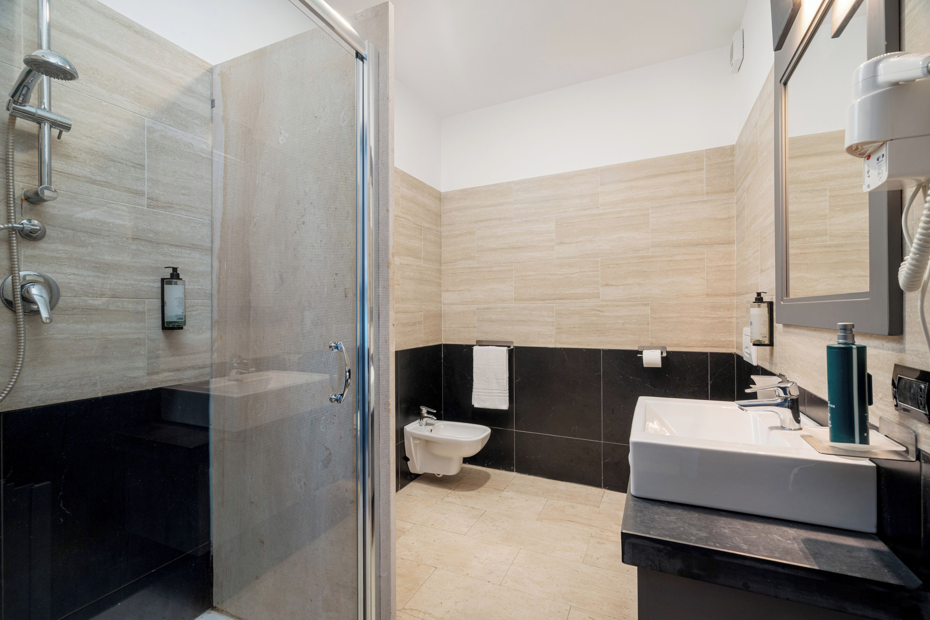 A modern bathroom with a glass-enclosed shower, a white sink, and a black-tiled wall.