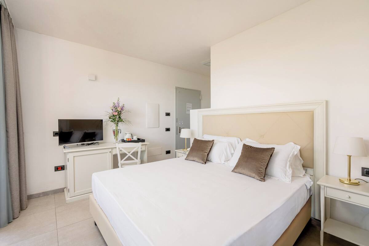 Une chambre d’hôtel avec un grand lit, un bureau avec une télévision, une lampe et un vase de fleurs.