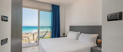 A hotel room with a large bed, a nightstand, a lamp, a view of the beach, and a sliding door.