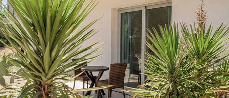A patio with a table and chairs, surrounded by various plants.