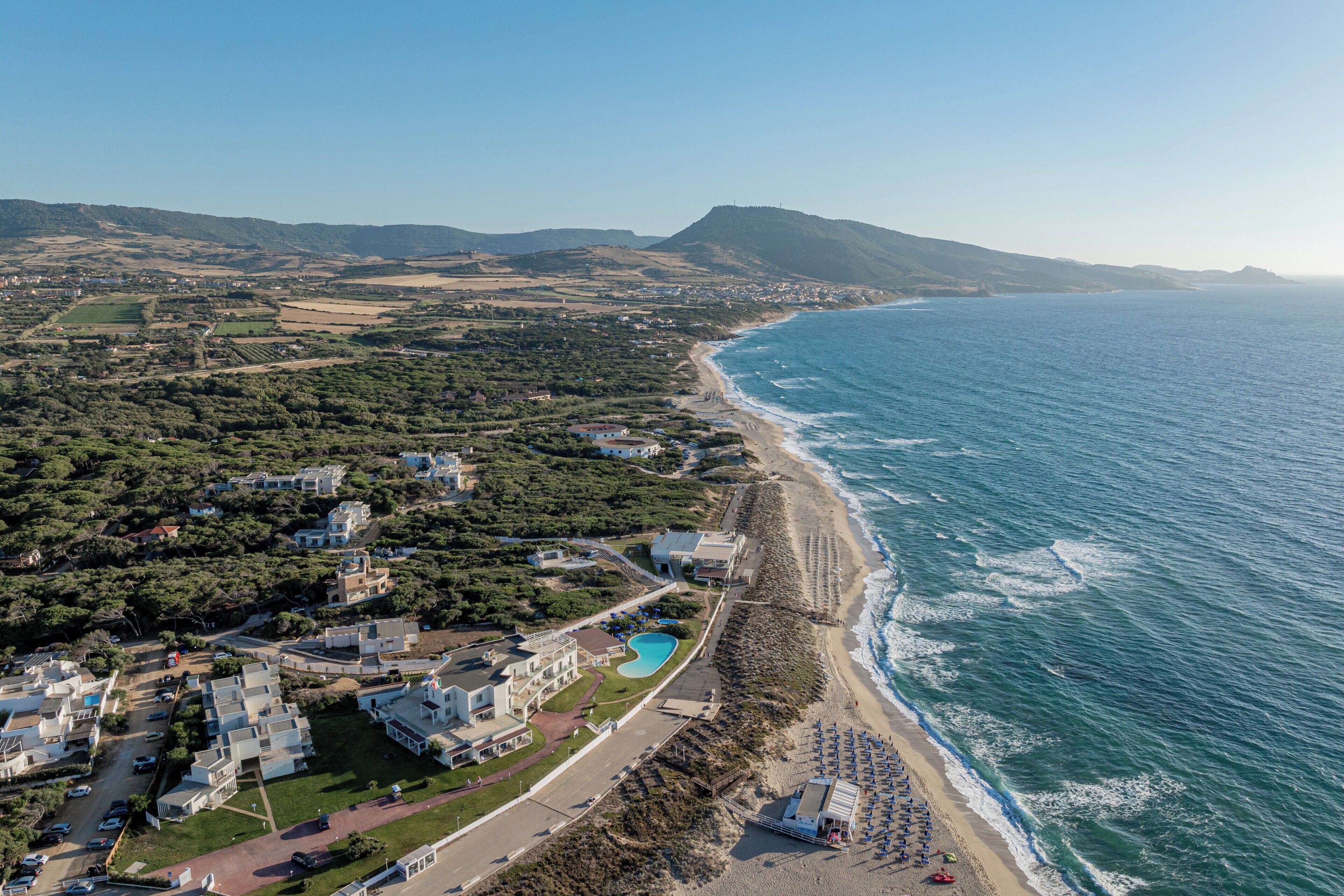 Oversigtsbillede af et kystområde med strand, swimmingpool og boligbygninger.